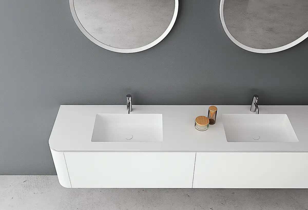 Vista superior de un mueble blanco de laterales curvos con doble lavabo integrado y dos espejos redondos