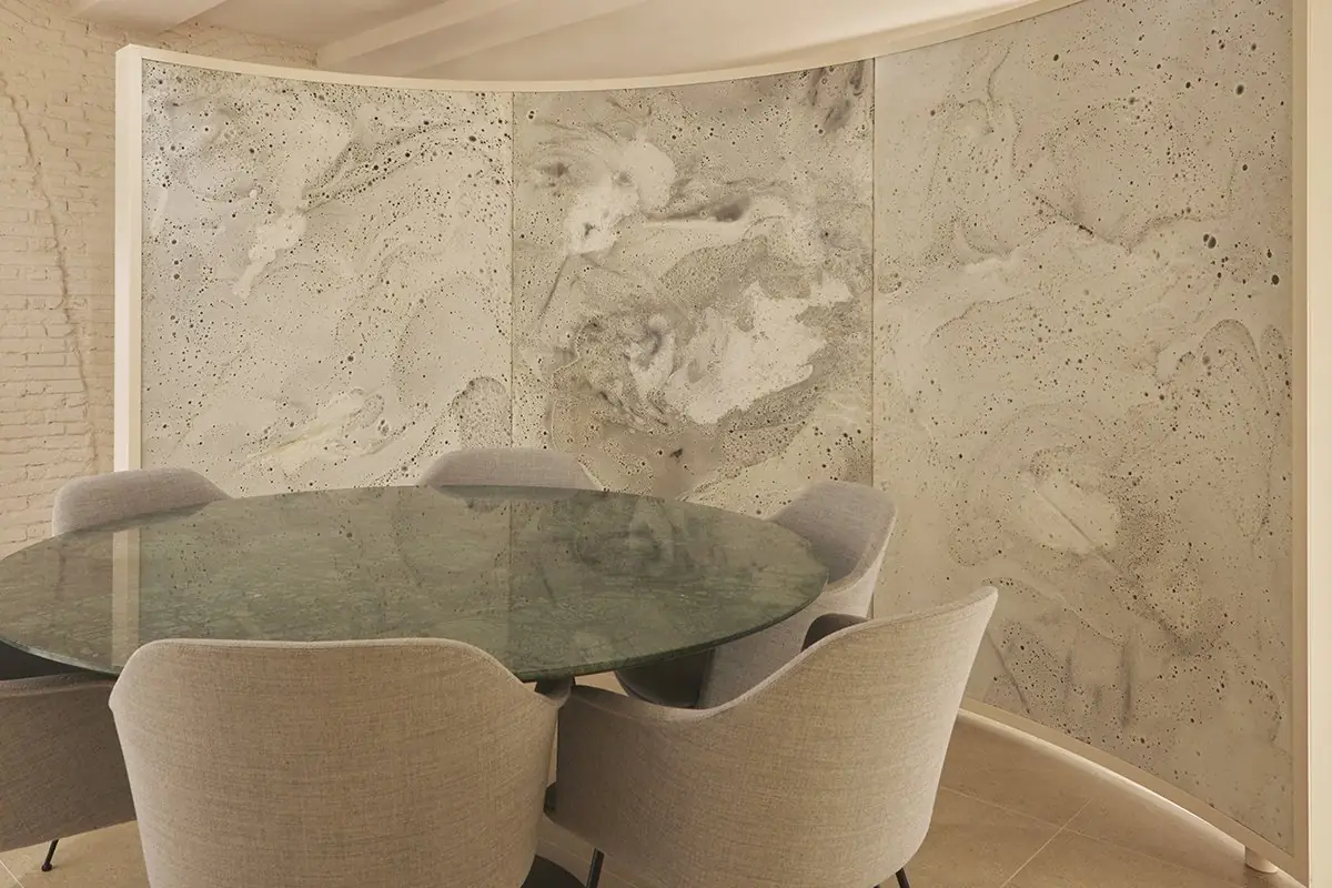 Meeting room with a round green table and upholstered chairs, enclosed by a curved screen of textured white material
