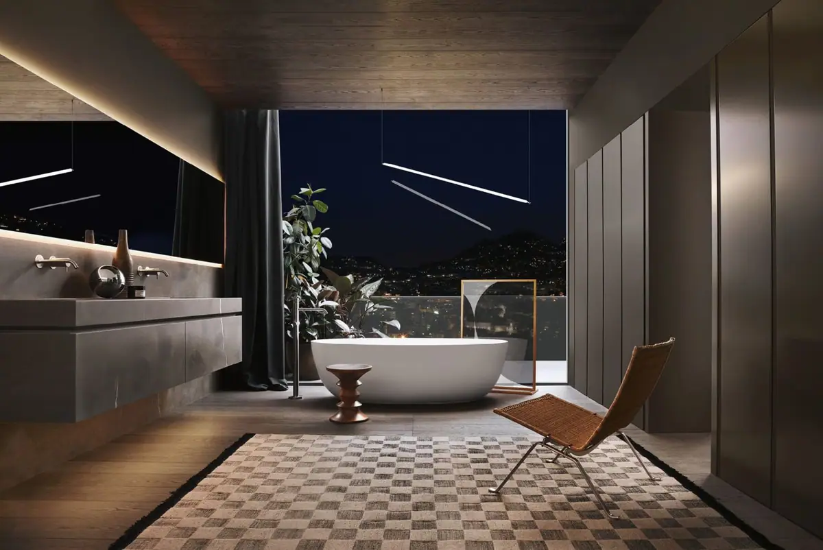 Baño nocturno con mueble largo de piedra oscura, columnas altas, bañera ovalada blanca exenta y un ventanal abierto a la ciudad.