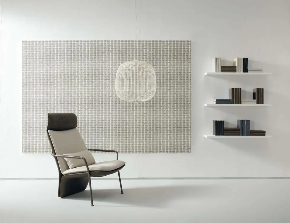 Panel of light-toned Matter Uren mosaic hung on the wall, with an armchair, a pendant lamp and white shelves.