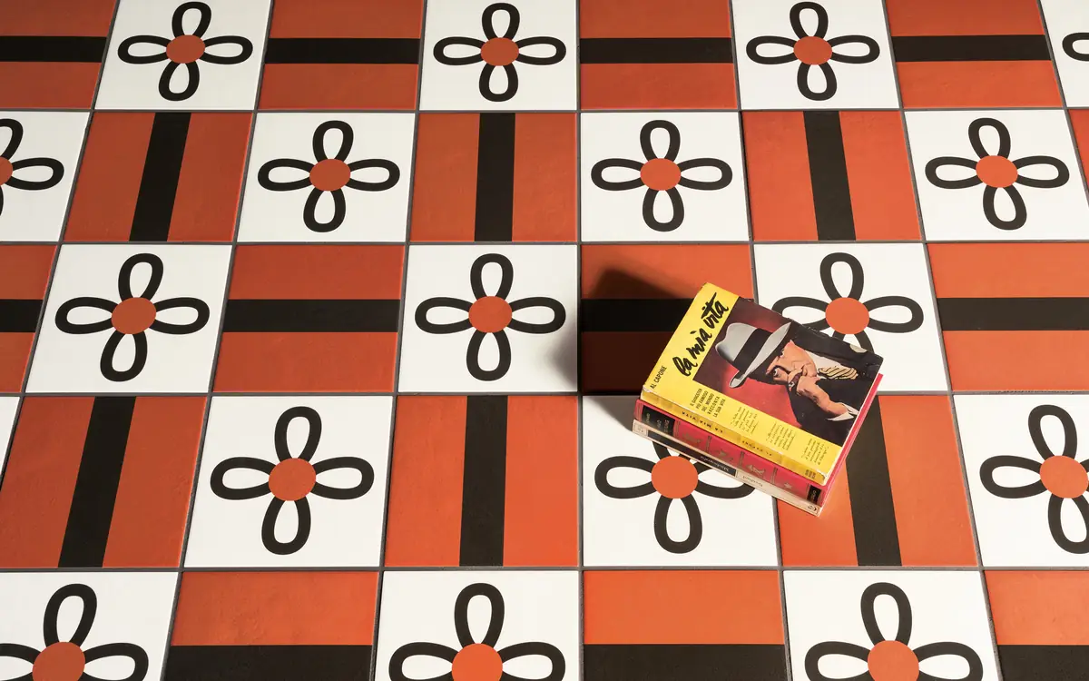 Floor of white tiles with black four-petal flowers and red centres, alternating with red pieces crossed by a black band