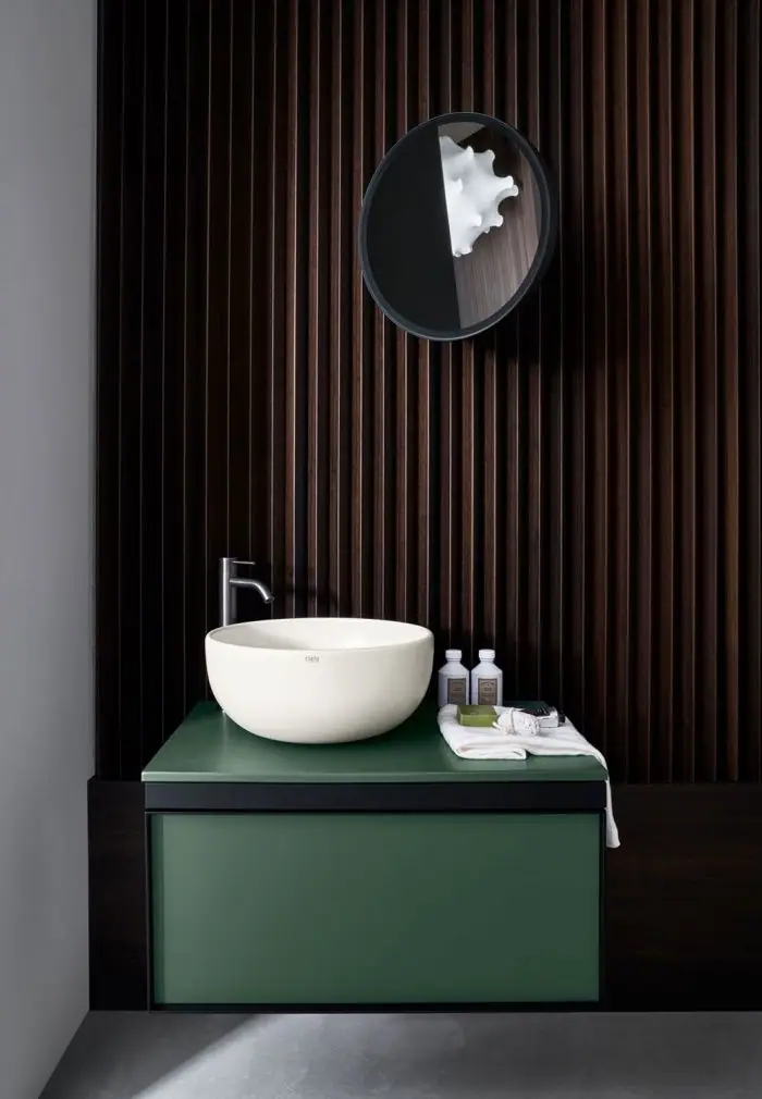 White countertop basin on a green countertop and green wall-hung unit with a drawer, against a wall of dark timber slats
