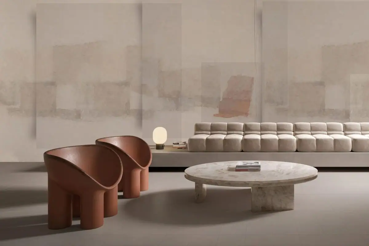 Living room with a modular sofa and reddish leather armchairs in front of a wall with abstract planes in cream and sand tones