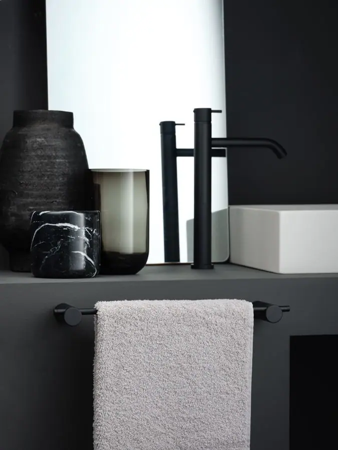 Toallero de varilla negra bajo una encimera gris con lavabo blanco y grifo alto negro