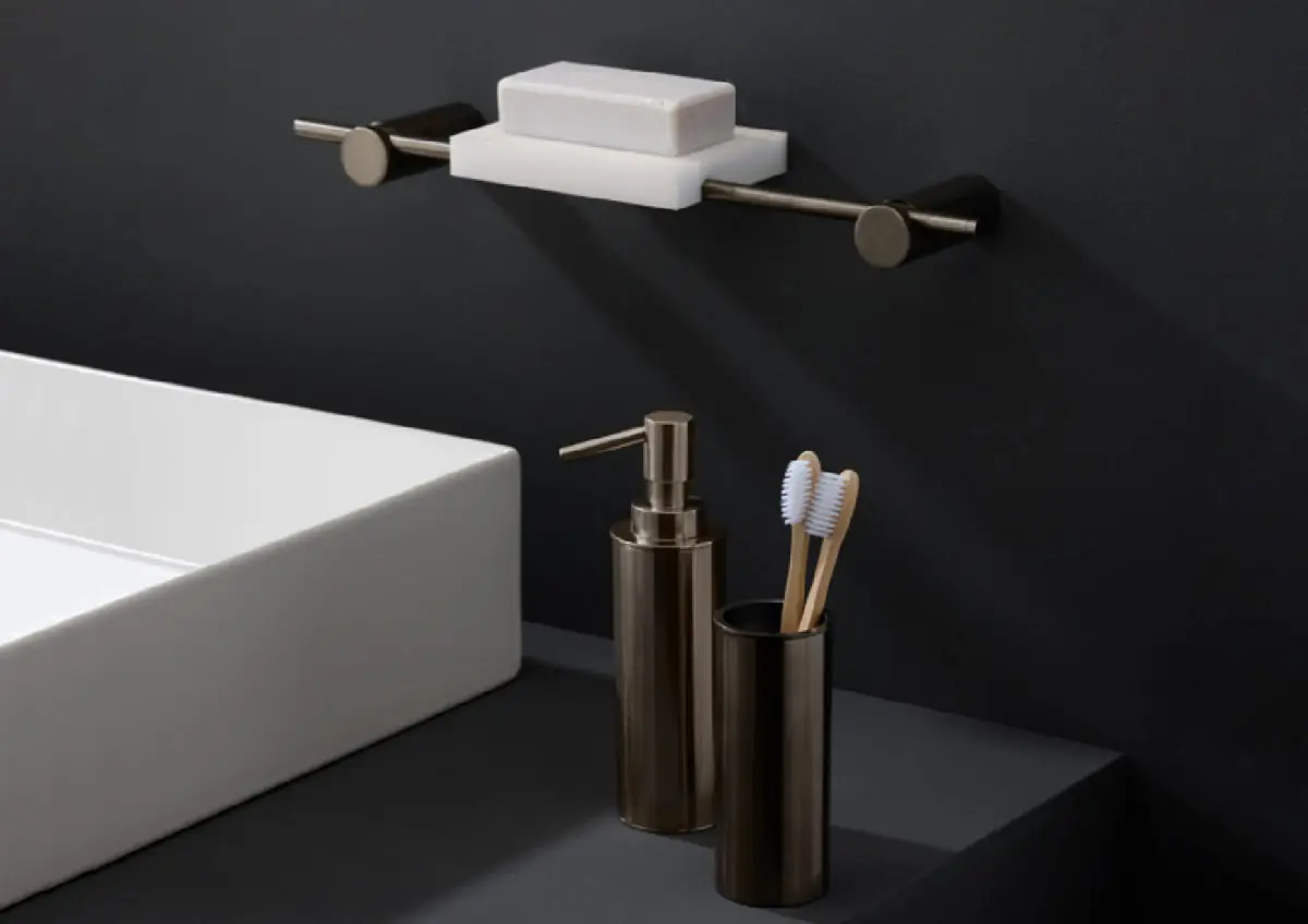 Estante blanco con una pastilla de jabón sobre una varilla metálica oscura, y dispensador y vaso metálicos junto a un lavabo