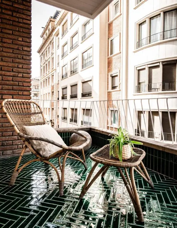 Terraza urbana con pavimento de piezas rectangulares verdes esmaltadas en brillo colocadas en espiga, un sillón y una mesa de ratán