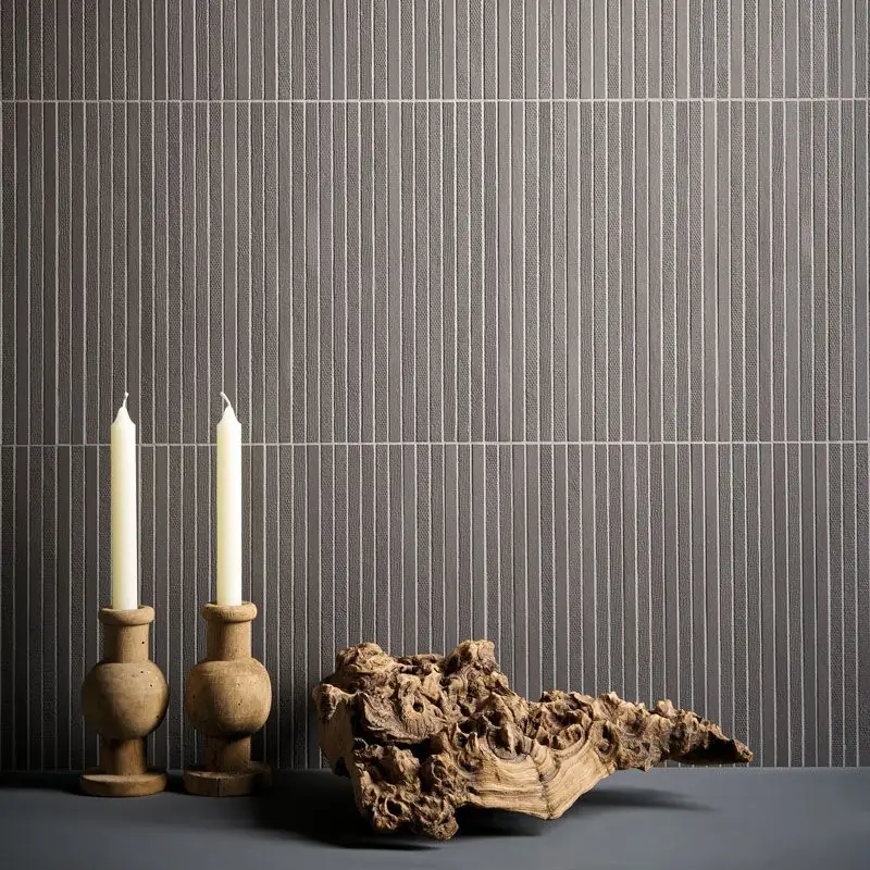 Pared revestida de listones cerámicos estrechos y verticales en gris, con juntas claras, y dos candelabros de madera delante