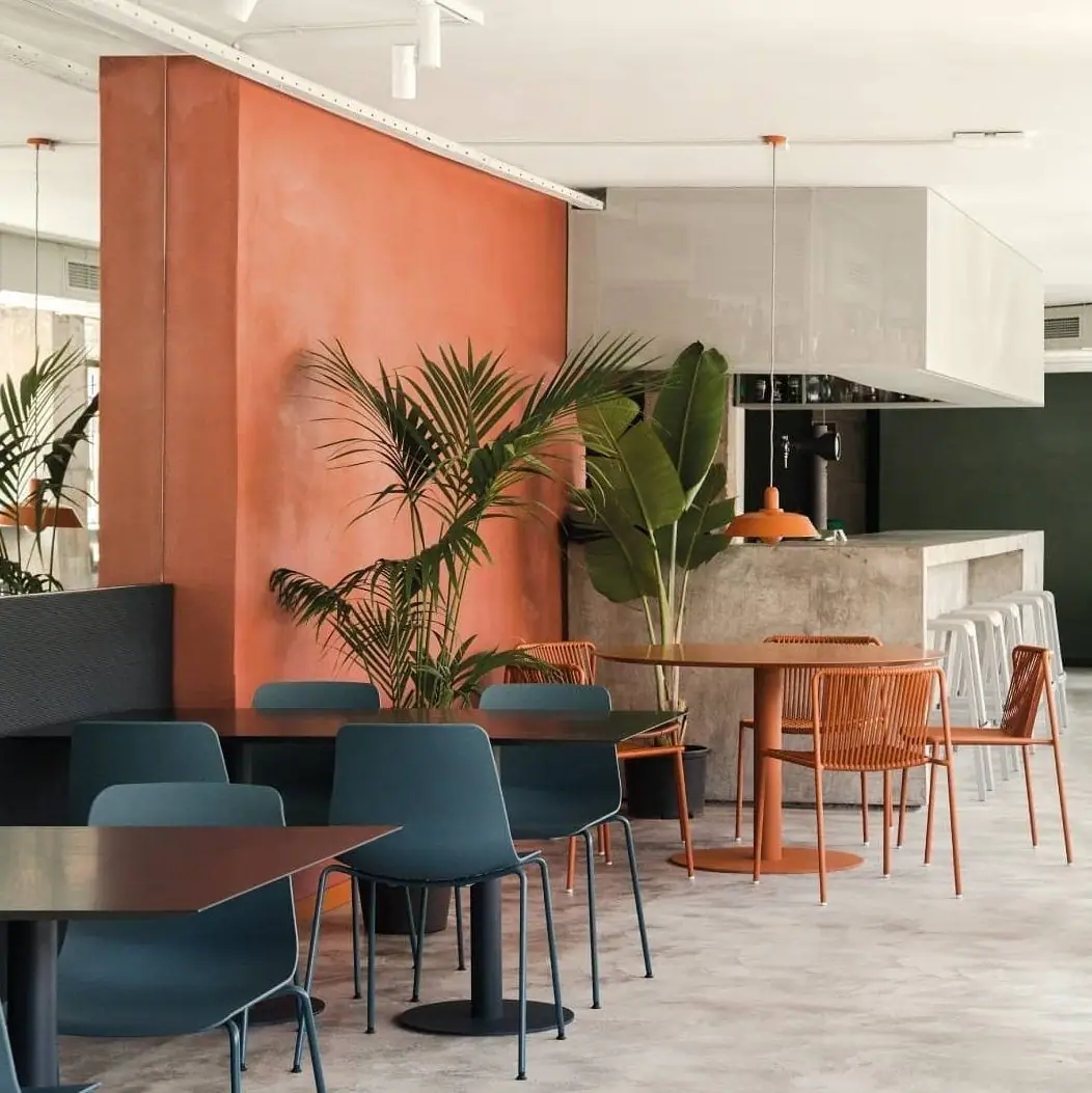 Bar restaurante con un gran paramento revestido de arcilla en tono terracota, mesas y sillas azules y naranjas y barra de hormigón