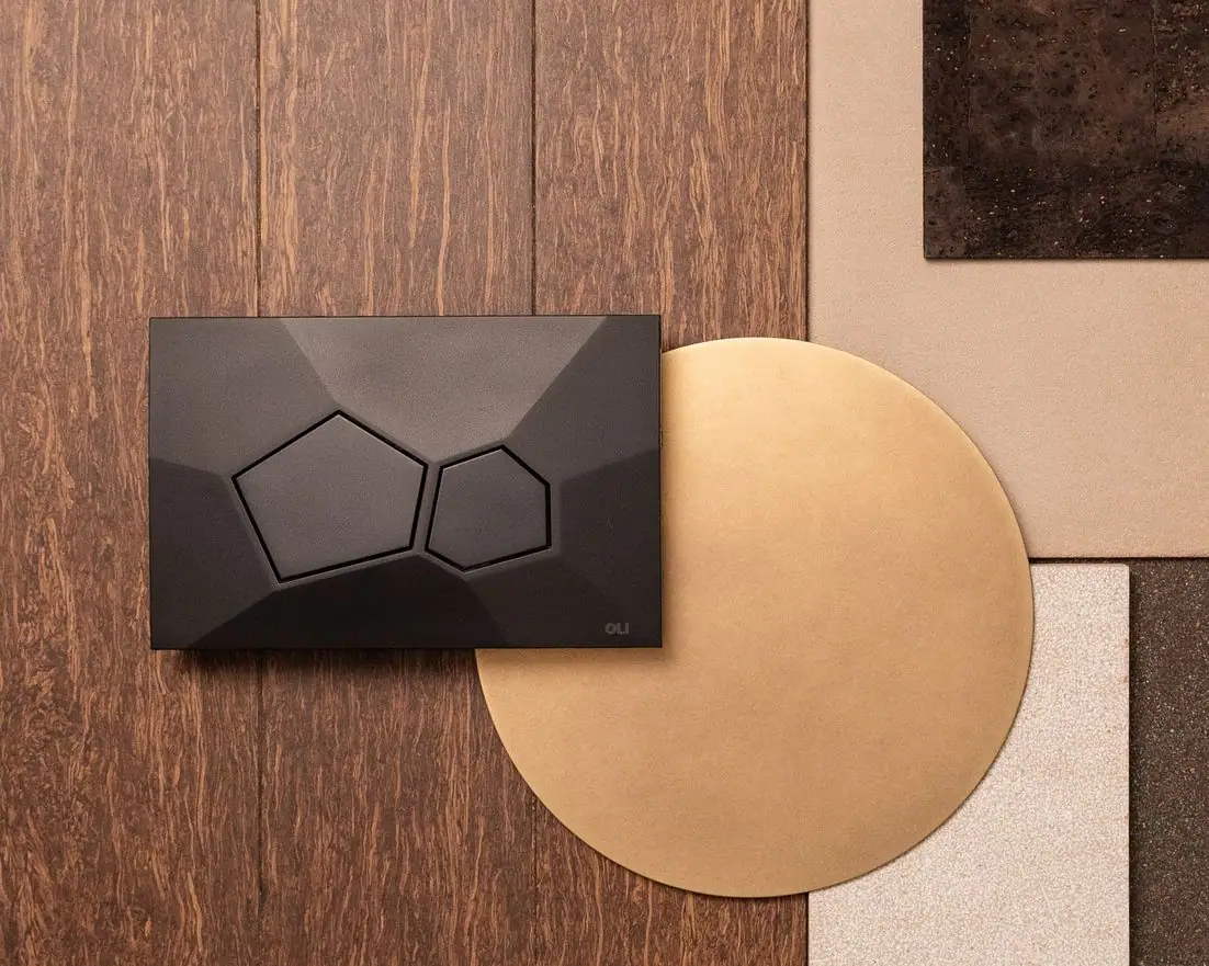 Pulsador VORONOI negro sobre tarima de madera, junto a un disco de metal dorado y muestras de corcho
