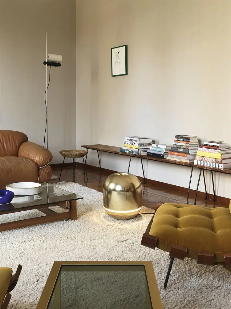 Calefactor esférico dorado EVE en el suelo de un salón, junto a una butaca de piel y una alfombra blanca