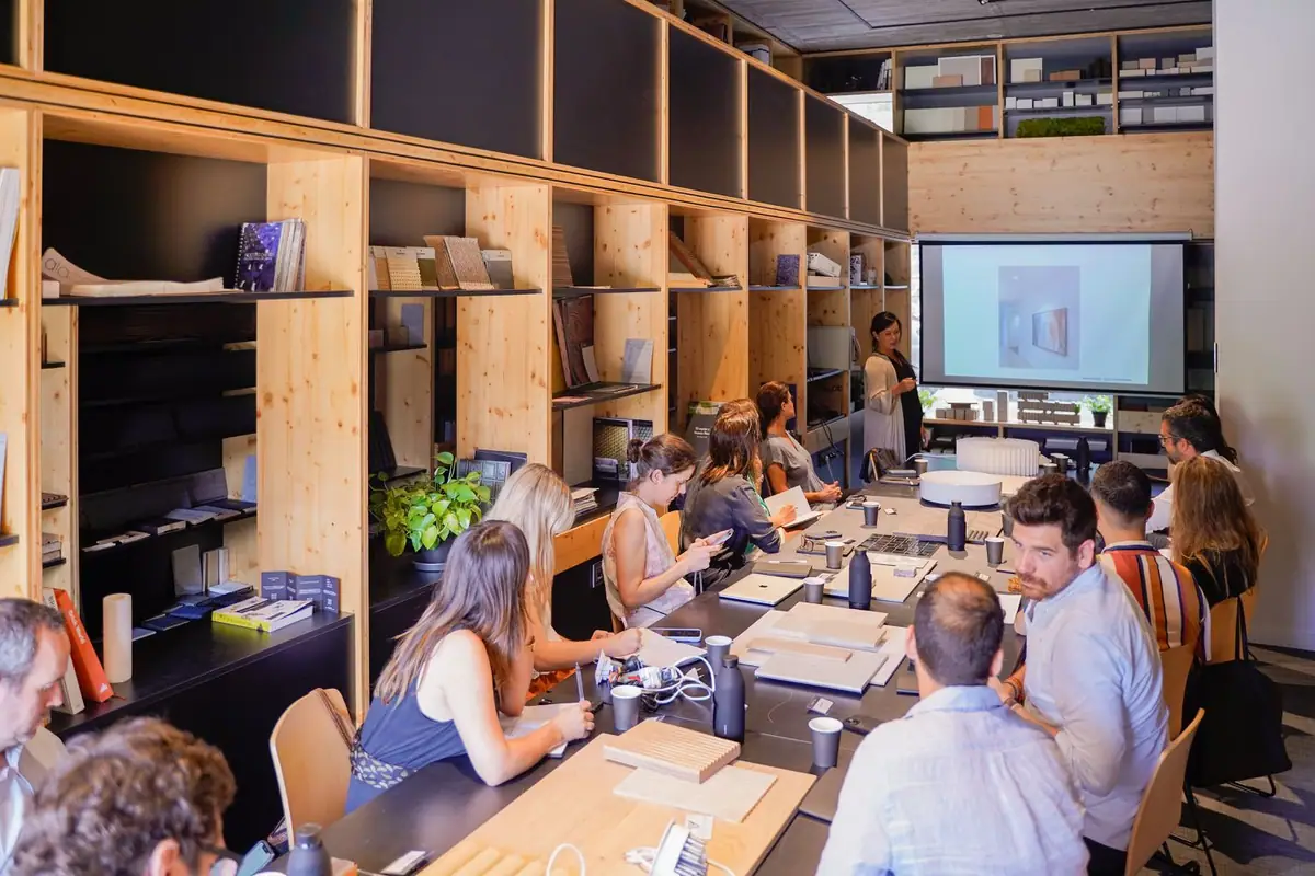 Asistentes sentados alrededor de una mesa con muestras de materiales mientras atienden a una presentación proyectada en la Materioteca de Matter Barcelona.