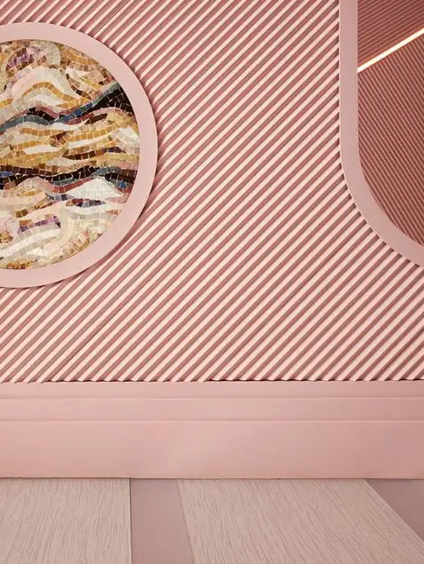 Detalle de una pared rosa con relieve diagonal, un mosaico circular y un zócalo del mismo color.