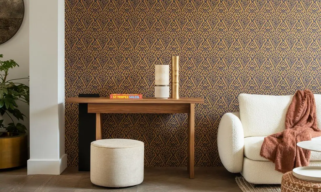 Wall covered in an ochre and blue geometric zigzag wallpaper, behind a wooden console and a white sofa