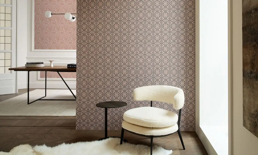 Room with a partition covered in wallpaper with small geometric motifs in pink and grey and a white armchair
