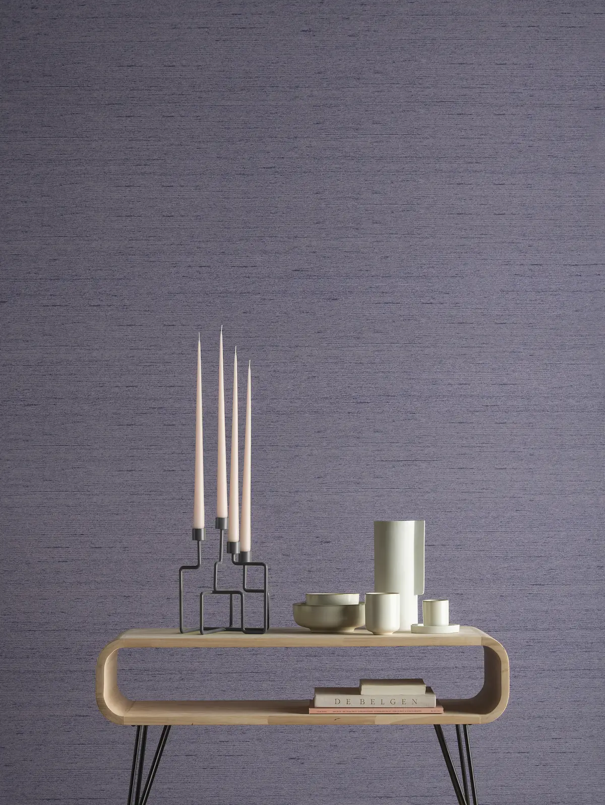 Consola de madera con velas y piezas de cerámica ante una pared revestida en violeta con textura de seda.