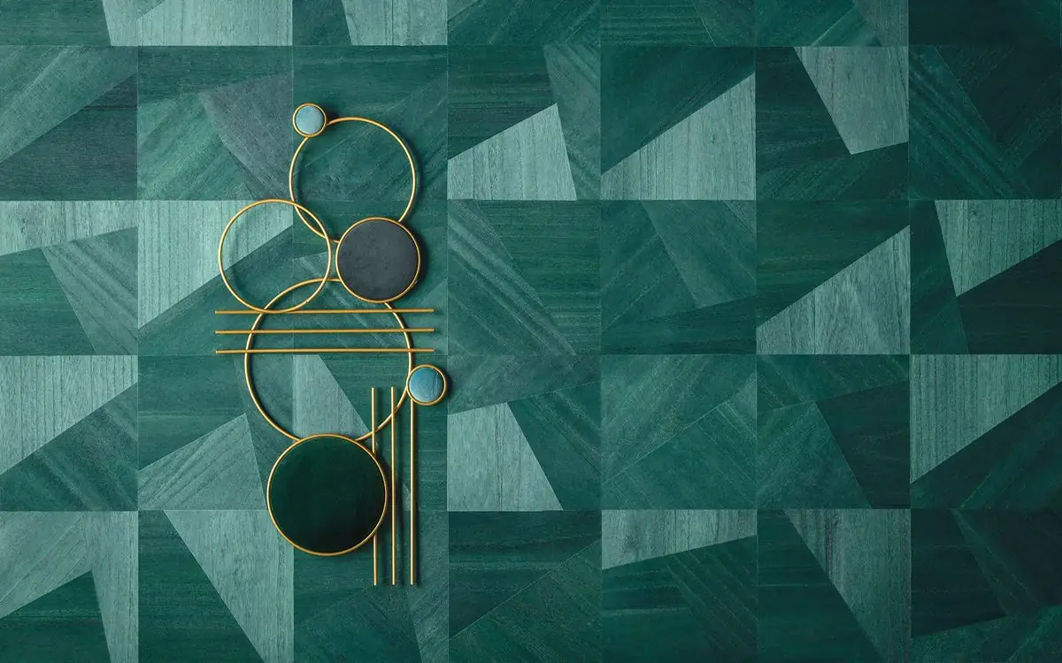 Revestimiento de marquetería de madera en tonos verdes con un mosaico geométrico de triángulos y cuadrados, y un objeto decorativo dorado.