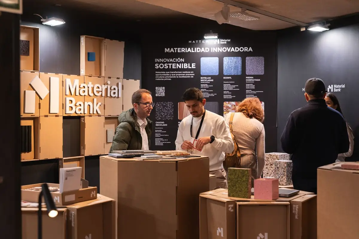 Two visitors talk in front of the Sustainable Innovation panel and a wall of boxes bearing the Material Bank logo