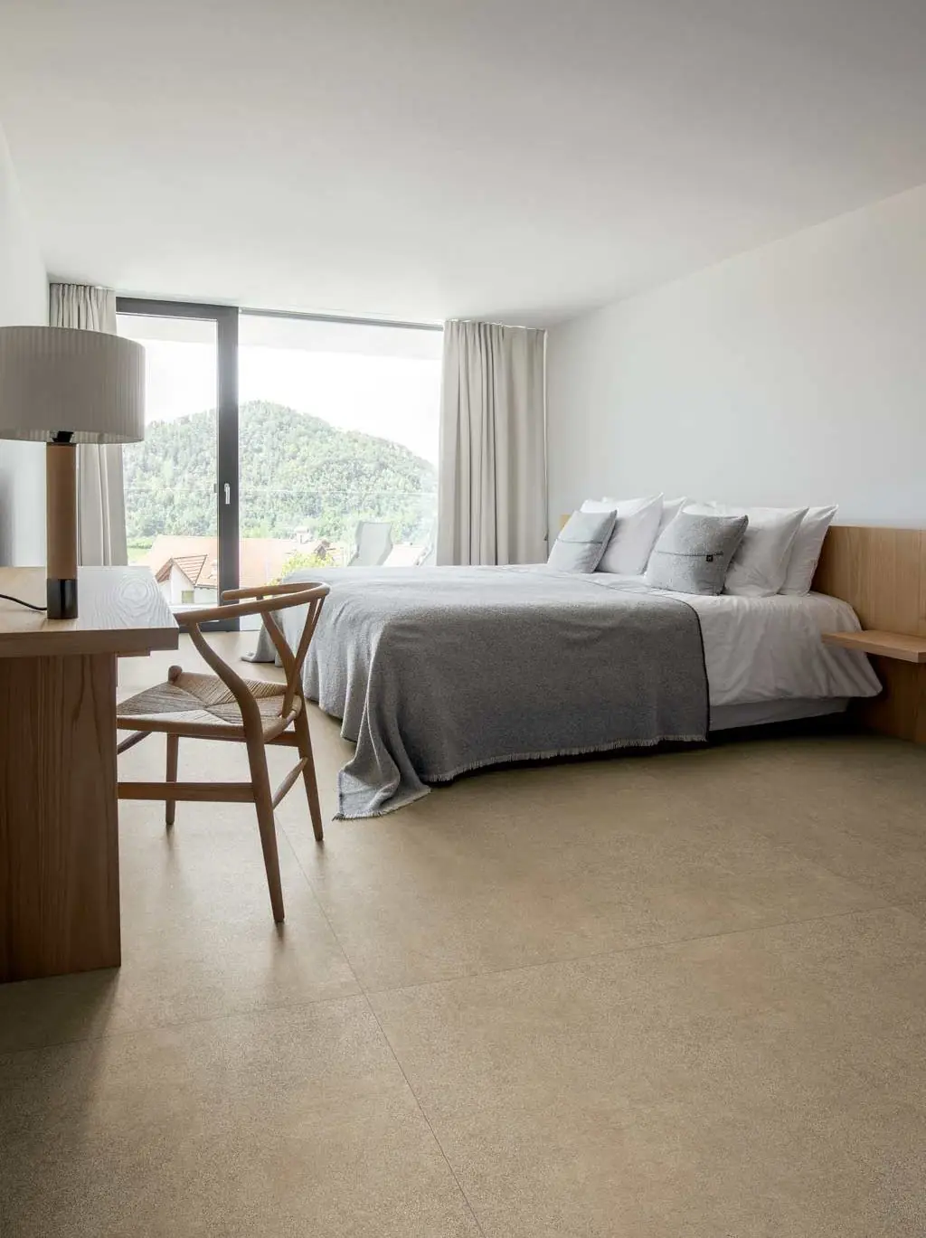 Dormitorio con cama, escritorio de madera y suelo de grandes baldosas de tono arena