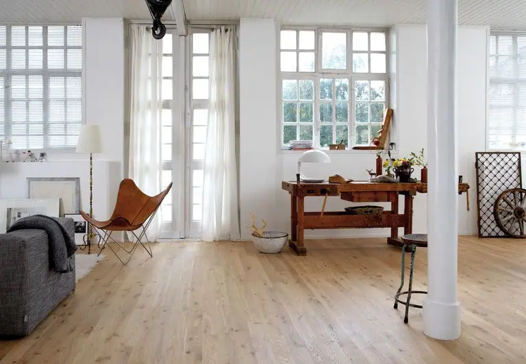 Open-plan living room with large windows, light wood flooring, a carpenter's workbench and a leather armchair