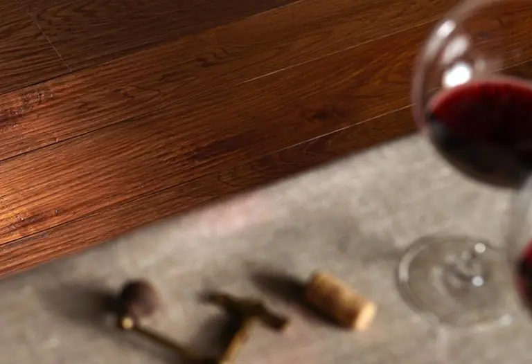 Warm-toned wood flooring next to a grey floor, with a glass of red wine, a corkscrew and a cork