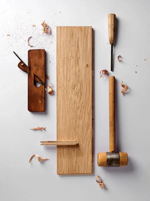Light oak board on a white background next to a carpenter's plane, a chisel, a mallet and wood shavings