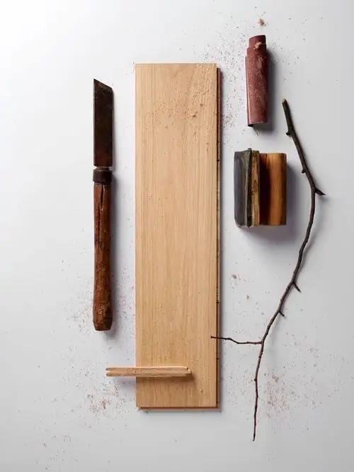 Light oak board on a white background, with a wooden-handled blade, wood chips and a branch