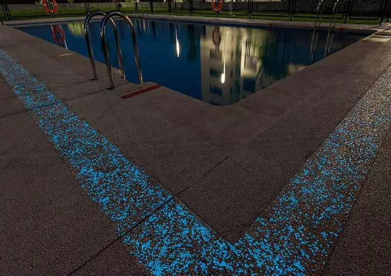 Piscina de noche con una franja de pavimento de hormigón que brilla en azul turquesa alrededor del vaso