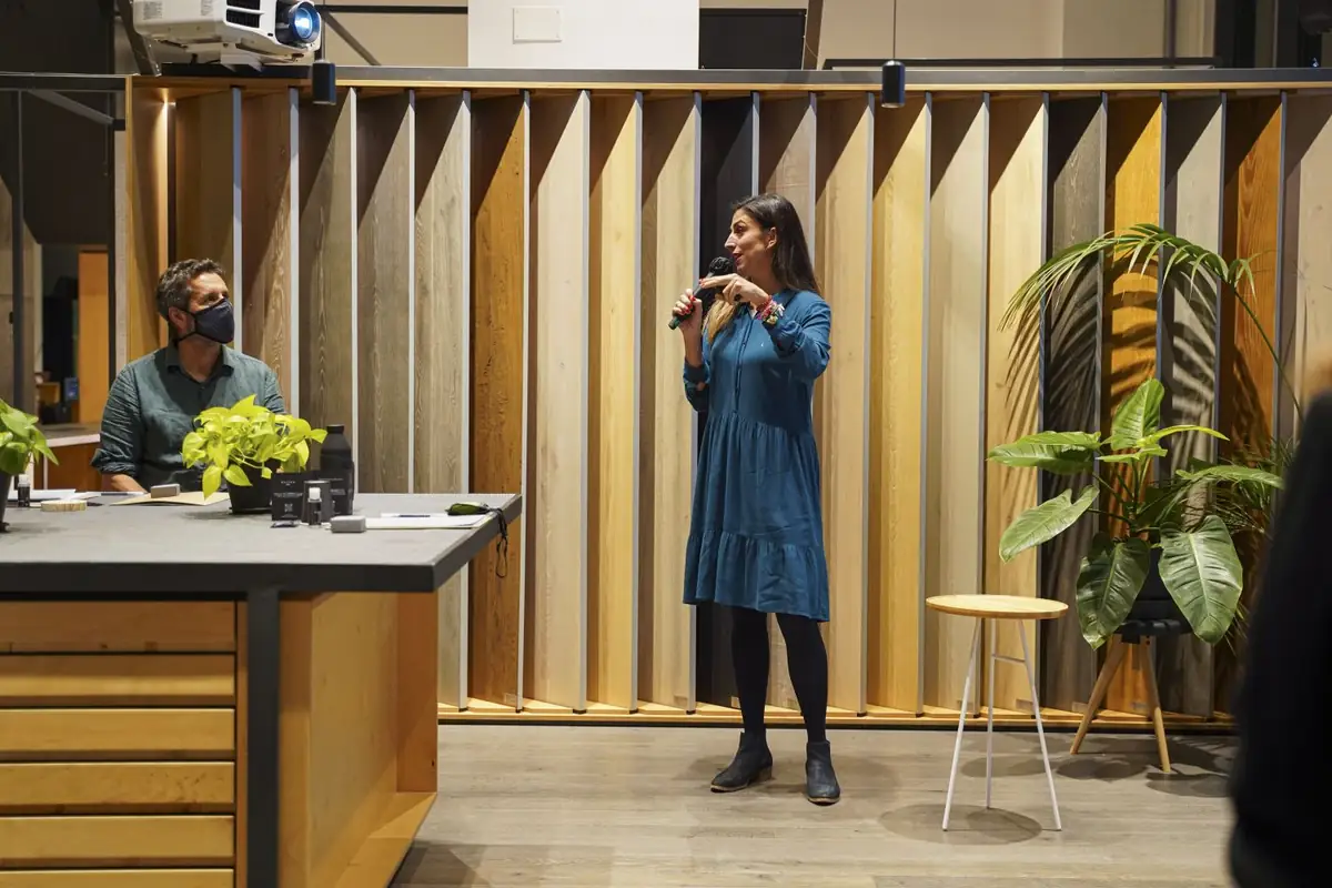 Una ponente con vestido azul habla con micrófono junto a la mesa de los ponentes