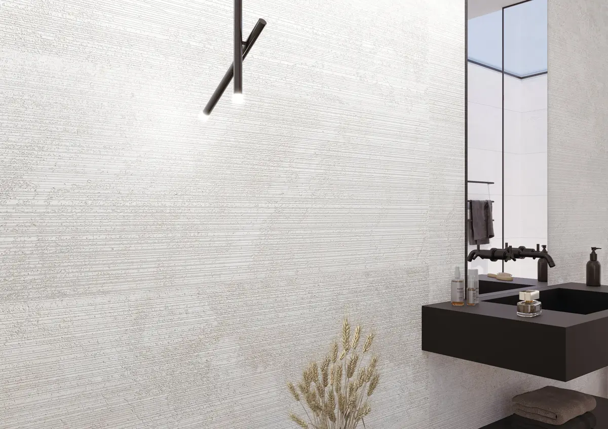 Pared blanca de efecto piedra con relieve de finas líneas horizontales y un taburete con toallas