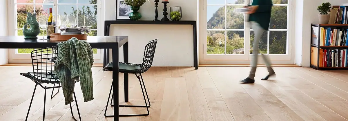 Comedor con suelo de tablones de roble claros, mesa negra, sillas de varilla metálica y grandes ventanales