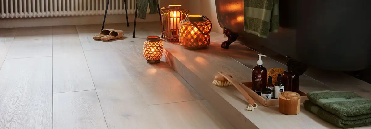 Suelo de tablones de roble en tono claro grisáceo con un escalón, faroles con velas y productos de baño