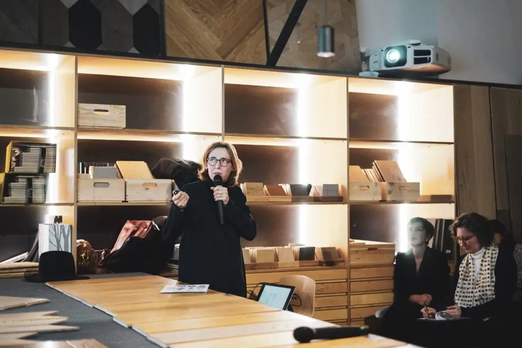 One of the invited architects speaks into a microphone beside the materials table while two others follow the talk seated