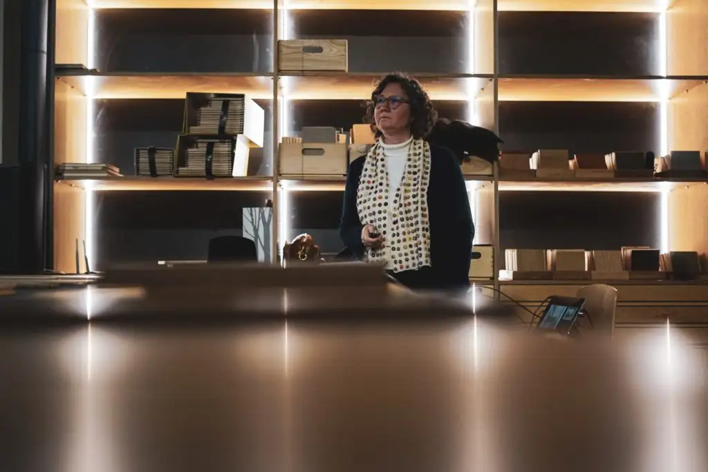 One of the invited architects, wearing a polka-dot scarf, listens standing in front of the illuminated shelves at Matter Barcelona