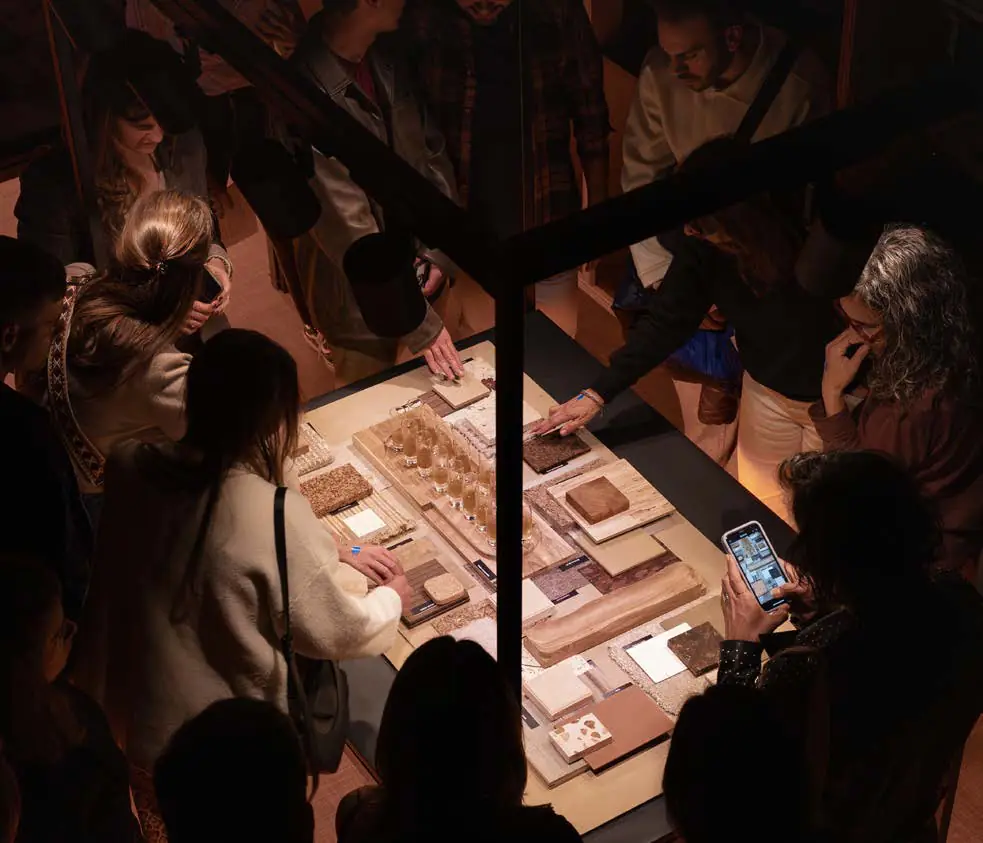 Vista cenital de asistentes alrededor de una mesa con muestras de materiales iluminada