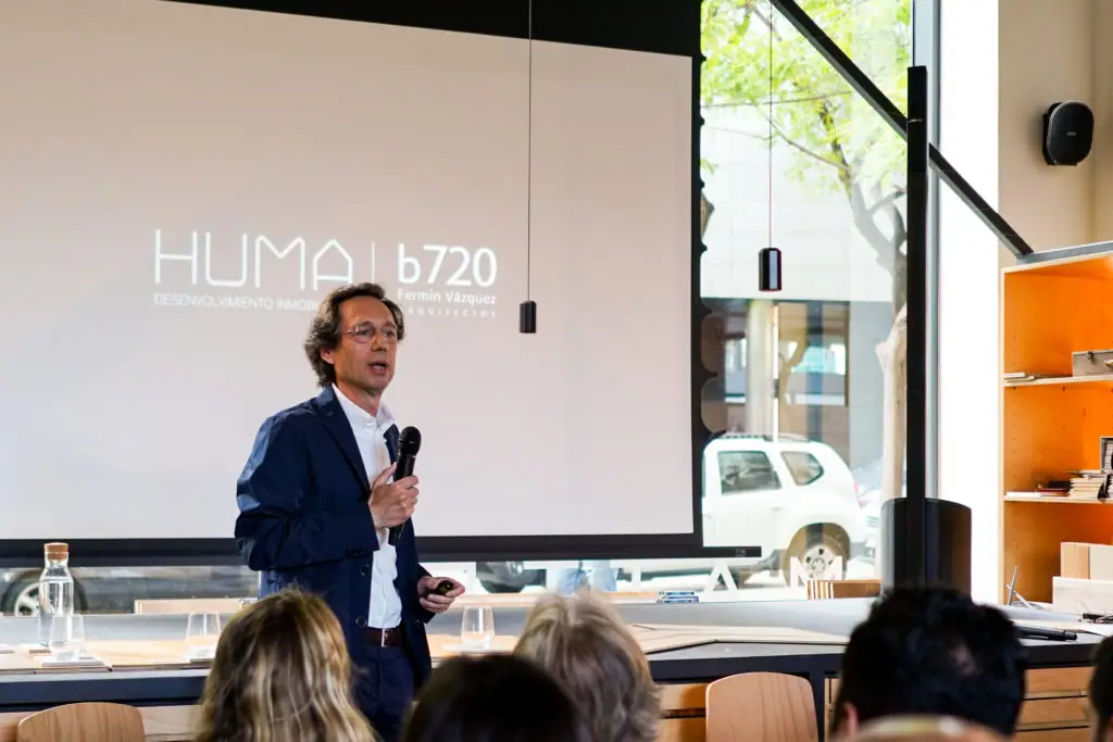 Fermín Vázquez habla con un micrófono ante una pantalla con los logotipos de Huma y b720 Fermín Vázquez Arquitectos