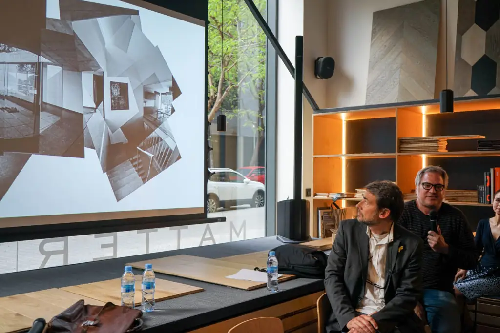 Screen with a projected axonometric drawing and speakers seated by the window at Matter Barcelona
