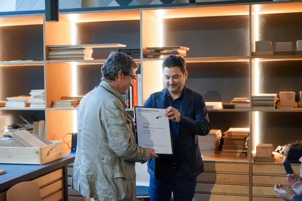 A man hands a framed diploma to another in front of the shelves at Matter