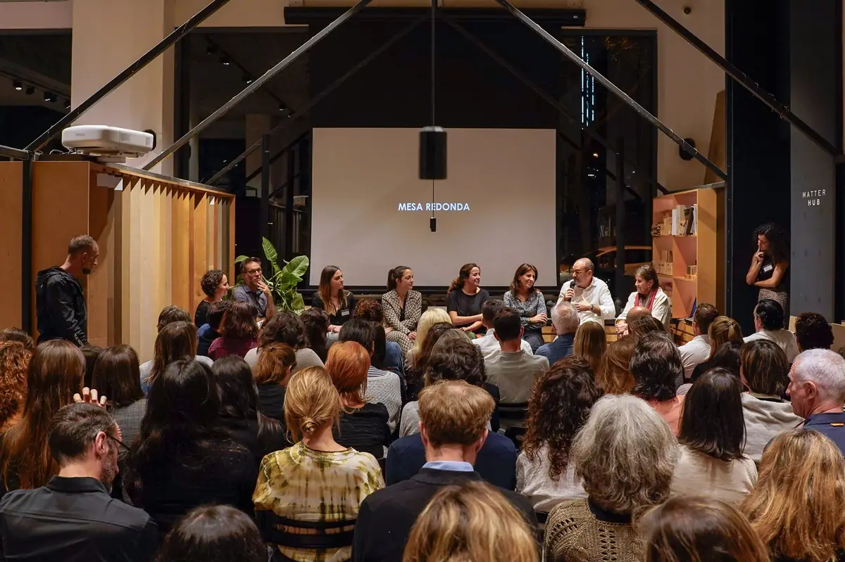 Público sentado ante la mesa redonda de ponentes, con la pantalla que anuncia la mesa redonda al fondo