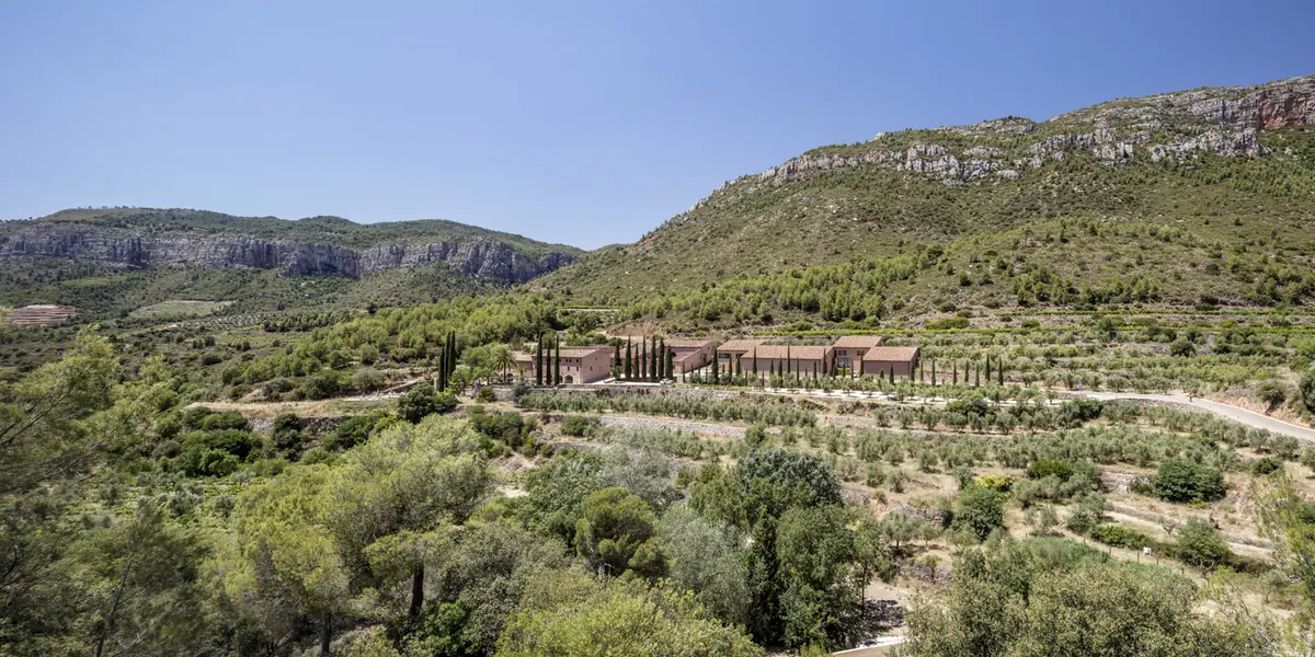Vista general de la finca entre olivos y matorral, con los edificios del hotel al pie de las sierras
