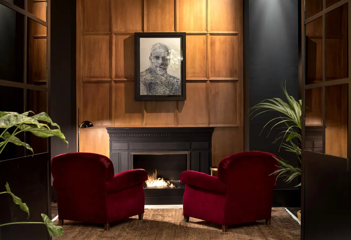 Living room with a fireplace, dark wood panelling, two red velvet armchairs and a framed portrait