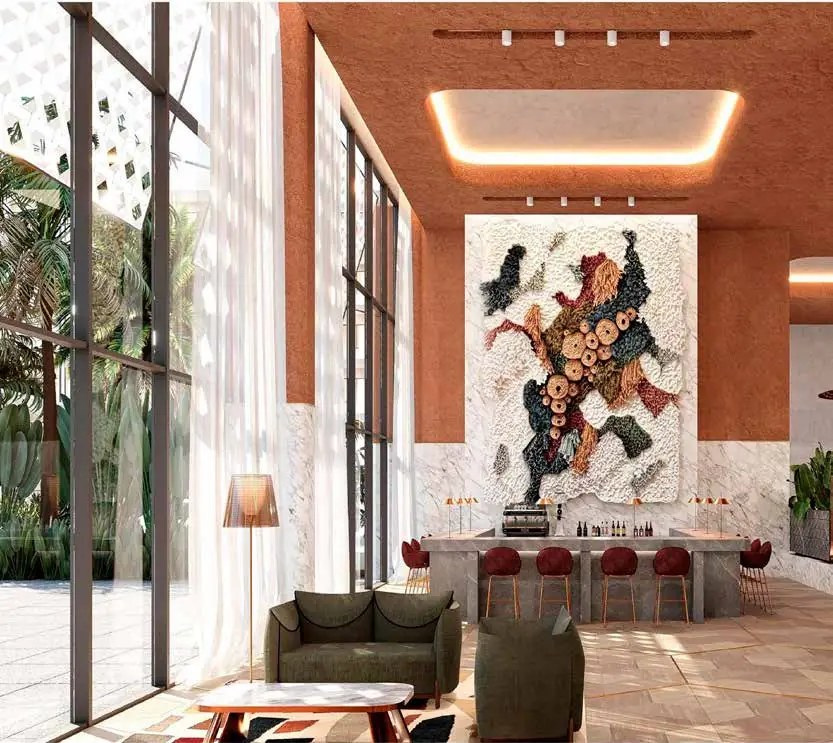 Double-height reception with terracotta-toned walls, a large textured textile hanging, green armchairs and a white lattice on the façade