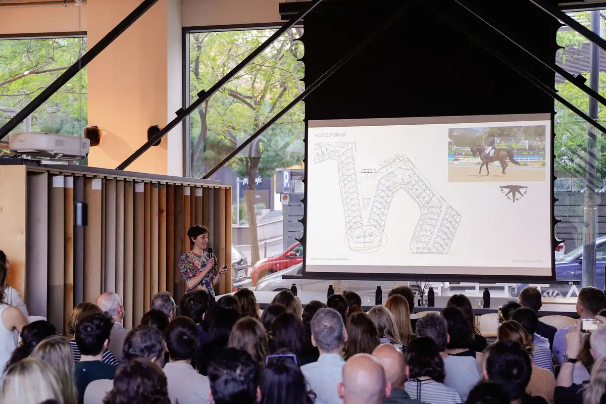 Ona Harster speaks beside a screen showing the hotel's sinuous plan and an image of a dressage horse
