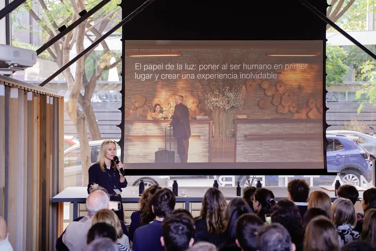Dolors Vila speaks into a microphone in front of a slide on the role of light in the guest experience