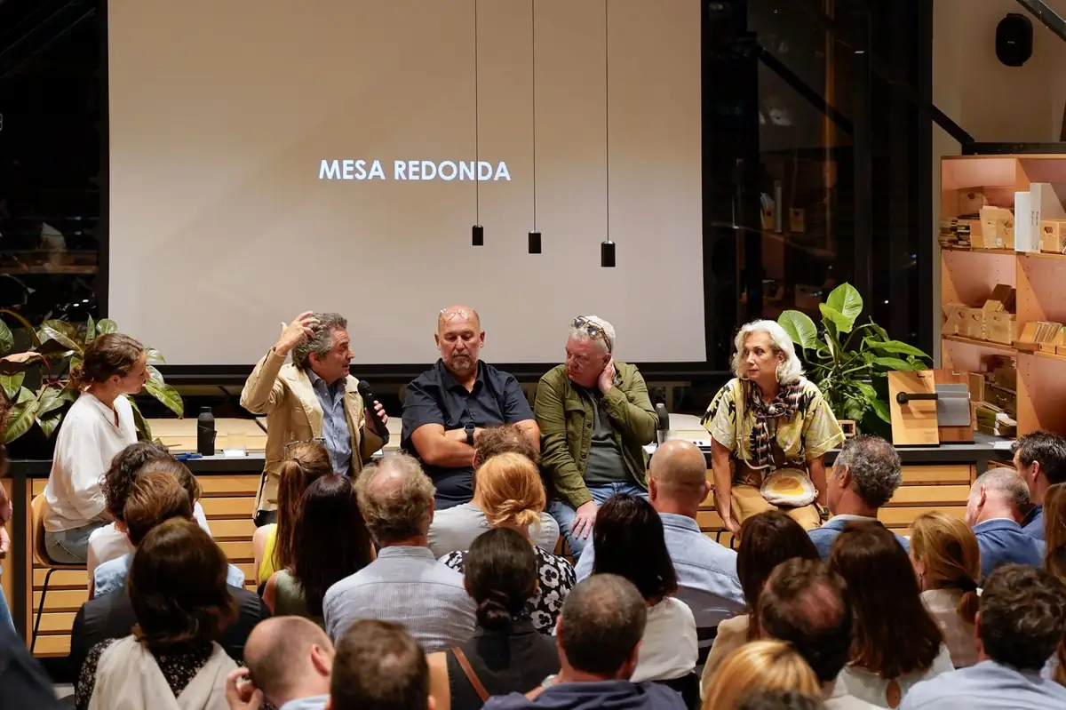 The speakers and moderator seated in front of a screen with the heading Mesa redonda (round table)
