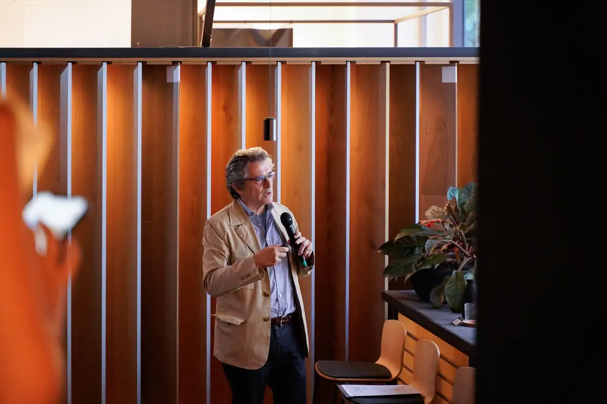 Felipe Pich-Aguilera speaks into a microphone in front of timber slat cladding