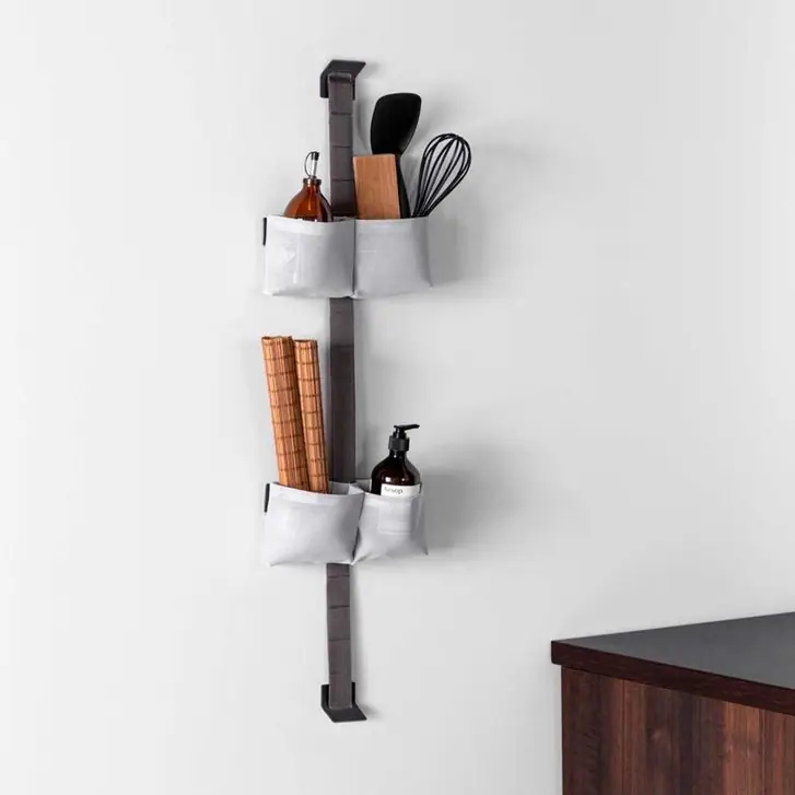 TAPE STORAGE strap on a kitchen wall with two grey double pouches holding utensils, oil and trivets