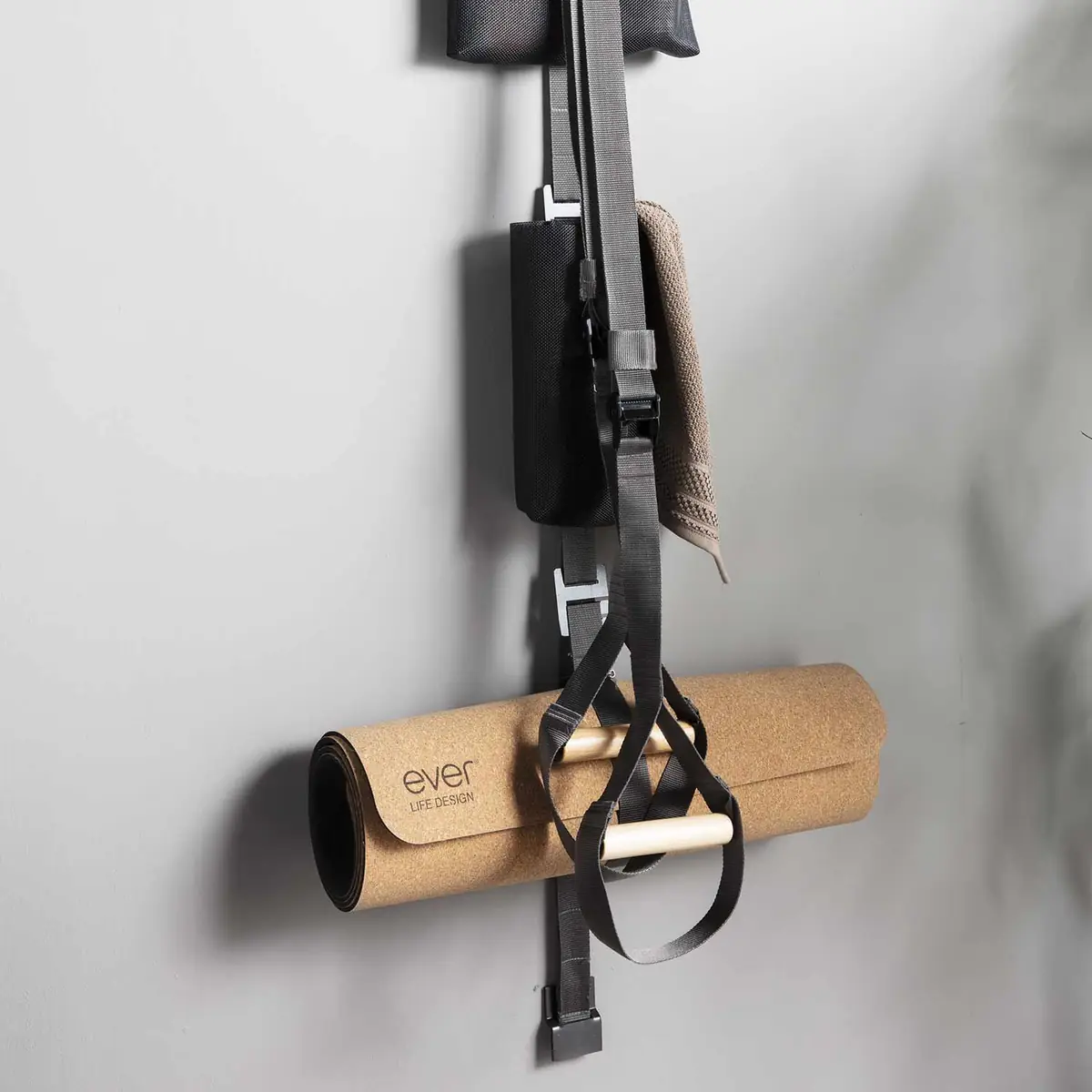 Rolled cork mat and training strap with wooden handles hanging from a TAPE strap on the wall