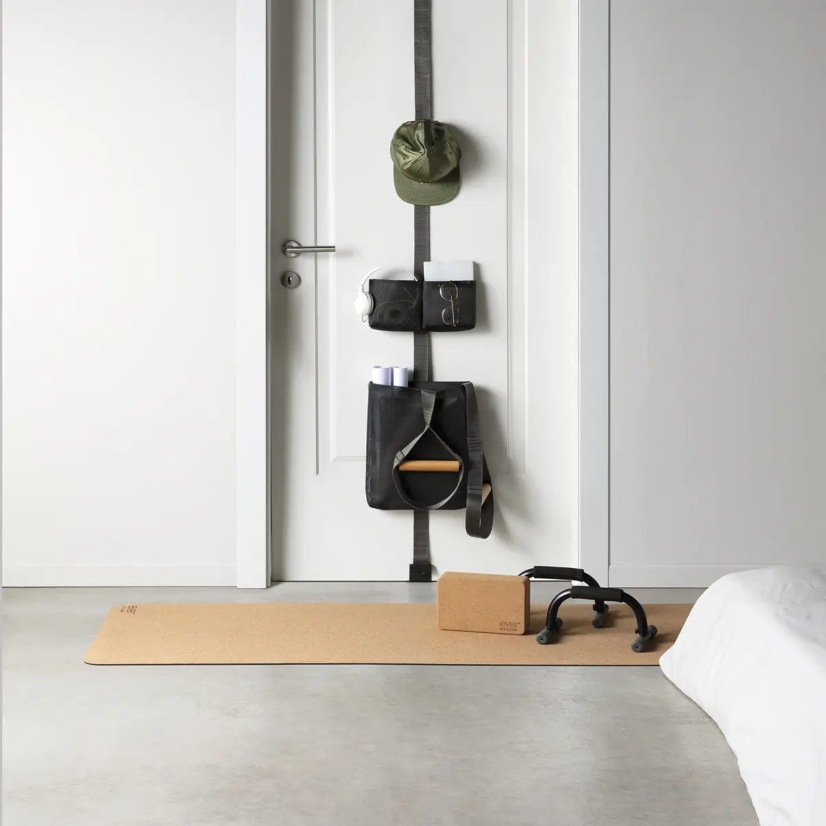 TAPE strap on a door with a cap, black pouches and a large bag holding training equipment, and a cork mat and block on the floor