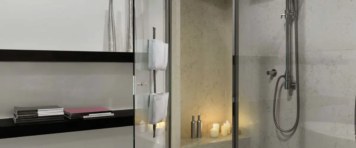 Shower with a glass screen and a TAPE SHOWER strap with grey pouches, next to a black shelf and candles