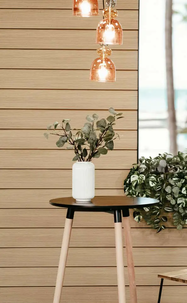Pared revestida de paneles horizontales de tono madera claro con una mesa auxiliar y lámparas colgantes